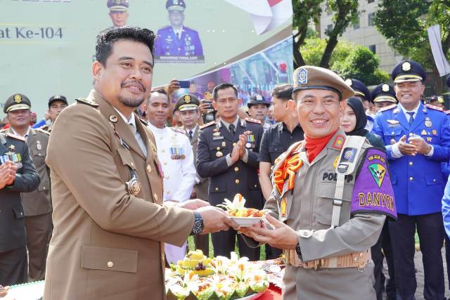 Wali Kota Medan, Bobby Nasution, memberikan potongan tumpeng kepada Kasatpol PP, Rakhmat AS Harahap, pada Peringatan HUT ke-73 Satpol PP di Lapangan Benteng Medan